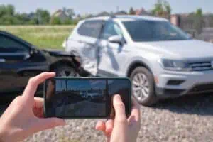 A person takes a photo of two damaged cars at the scene of a traffic accident, with both vehicles showing visible collision damage.