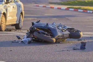 A damaged motorcycle lies on its side in the road next to a dented car, suggesting a recent traffic accident at an intersection.