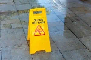 A yellow caution sign reading "Caution Wet Floor" stands on a wet tiled floor.