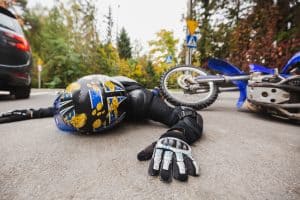 A motorcyclist wearing a blue helmet and gloves lies on the road next to a fallen motorcycle after an apparent accident.