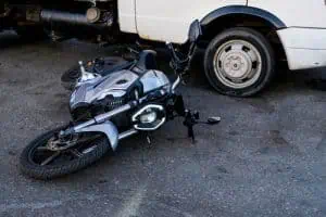 A motorcycle lying on its side next to the rear wheel of a white van on a paved surface.