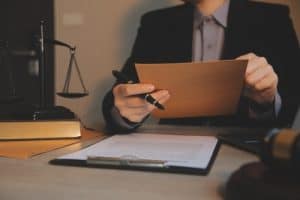 Person in business attire reviews a document at a desk with legal scales, a gavel, and paperwork.