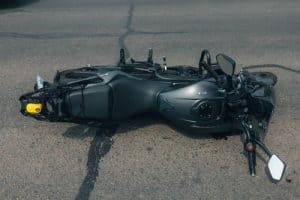 A black motorcycle lies on its side on an asphalt road, showing signs of a recent accident.