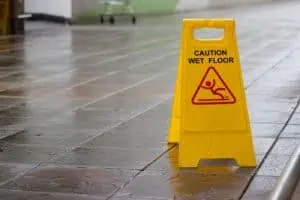 A yellow "Caution Wet Floor" sign stands on a shiny, wet tiled floor indoors.