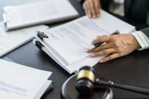 A person reviews and signs legal documents at a desk with a gavel and paperwork.