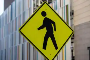 Yellow pedestrian crossing sign with a black walking figure in front of a building with vertical colorful lines.
