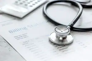 A stethoscope and a calculator rest on a medical billing statement listing services and charges.