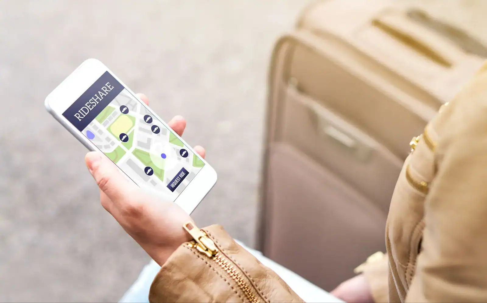 Person holding a smartphone with a rideshare app open, showing a map and ride options, next to a beige suitcase.