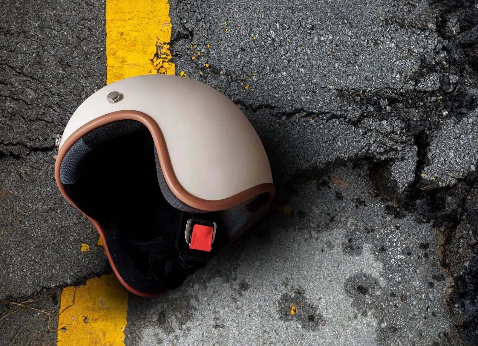 A motorcycle helmet lies on cracked asphalt near a yellow line.