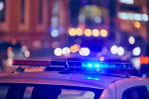 The roof of a police car with blue and red emergency lights flashing at night, with blurred city lights in the background.