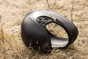 A cracked and damaged black motorcycle helmet lies on dry, yellow grass.